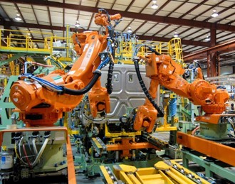 Orange robotic arms assemble Freightliner Cascadia components on an assembly line
